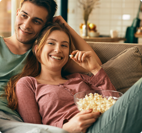 Photo of a man and a woman watching TV and eating popcorn