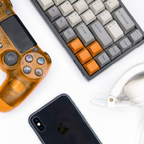 Overhead view of an orange PlayStation controller, keyboard, headphones, and a smartphone
